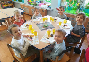 Dzieci przy stoliku degustują ciasteczka w wielkanocnych kształtach.